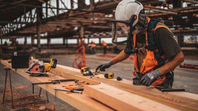 man in orange and black vest wearing white helmet holding yellow and black power tool
